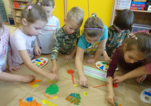 Siedmioro dzieci stempluje pomponami maczanymi w farbie sylwetę motyla.